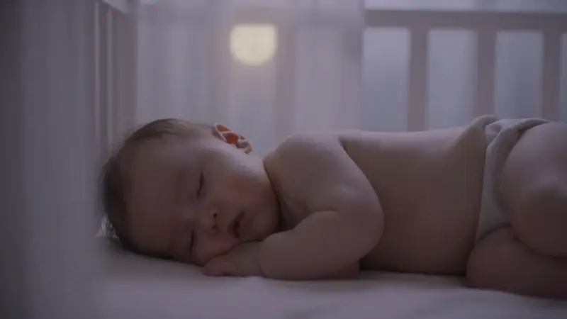 Bebé durmiendo en una posición inusual en un cuarto infantil tenuemente iluminado por la luz de la luna. Ambiente onírico y suave.