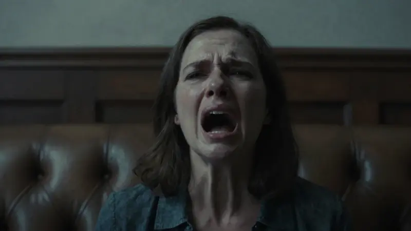 Primer plano de rostro femenino con expresión de frustración y un grito silenciado, en un consultorio psicoanalítico tenuemente iluminado con un diván de cuero antiguo.