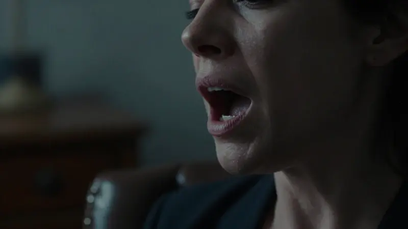 Primer plano de rostro femenino con expresión ansiosa, en una consulta psicoanalítica con ambiente tenue y melancólico. La mujer parece intentar gritar en silencio.