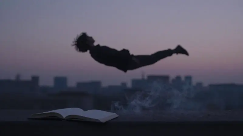 Figura silueteada flotando sobre una ciudad crepuscular, con un diario abierto cerca y una atmósfera melancólica.