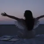 Mujer con alas volando silueteada contra el cielo crepuscular, observando un dormitorio con diarios de sueños y una taza de té.