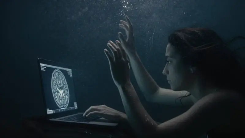 Figura sumergida en aguas turbias, con las manos extendidas hacia la superficie y un reflejo distorsionado. Una pantalla de portátil muestra imágenes de escáneres cerebrales en el fondo.