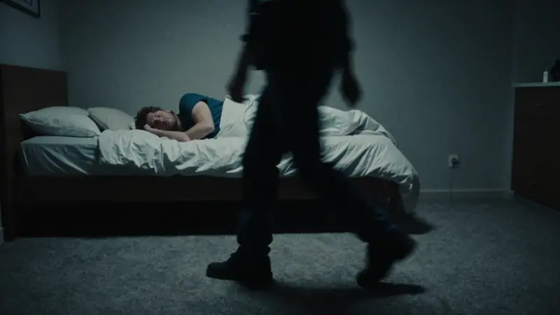 Escena del crimen con un hombre sonámbulo avanzando en un dormitorio tenuemente iluminado, rodeado de elementos forenses y sombras.