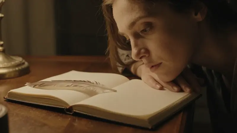 Mujer pensativa frente a un escritorio antiguo con un diario de sueños abierto y una pluma de águila en foco suave.