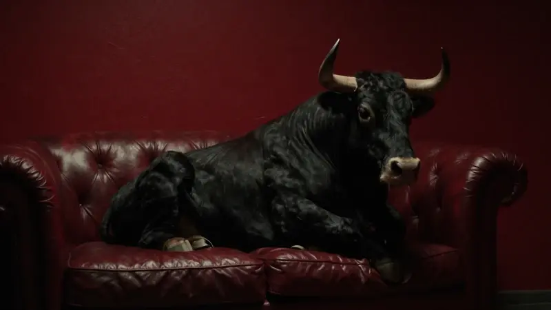 Toro imponente en una atmósfera que evoca un consultorio de psicoanálisis tenuemente iluminado, con un sofá de cuero y una paleta de colores rojos y negros melancólicos.