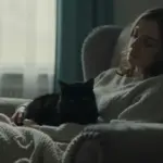 Mujer durmiendo en un sillón con un gato negro acurrucado en su regazo, en un estudio íntimo y suavemente iluminado.