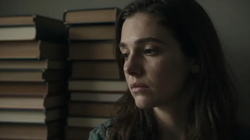 Mujer pensativa en una habitación oscura con estanterías llenas de libros antiguos, evocando una atmósfera introspectiva relacionada con la interpretación de los sueños.