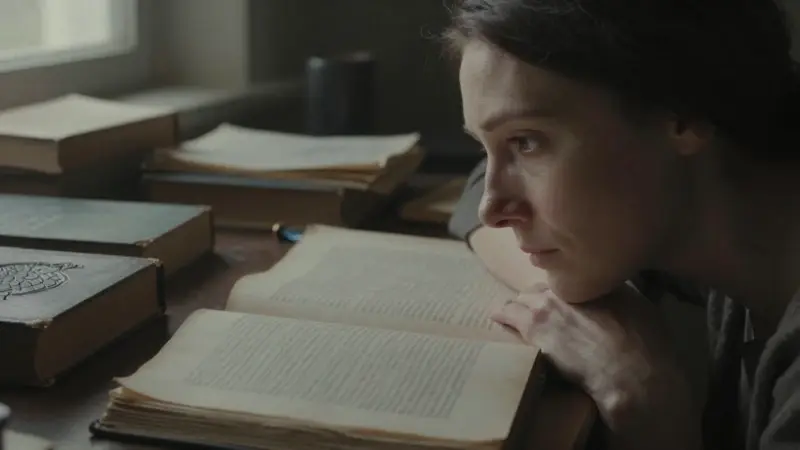 Mujer pensativa en un estudio antiguo, rodeada de libros sobre análisis de sueños y mitología. Un patrón de escamas de dragón se vislumbra en la portada de uno de los libros.