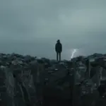 Figura solitaria frente a un profundo abismo rocoso bajo un cielo tormentoso y nublado.