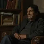 Escritor peruano en estudio con estanterías repletas de libros, iluminado tenuemente en una atmósfera melancólica y contemplativa.