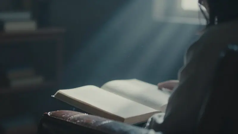 Figura pensativa en un estudio tenuemente iluminado, frente a un libro abierto, evocando un ambiente de introspección y sueños.