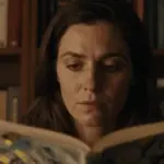 Mujer pensativa en estudio con libros de psicología y análisis de sueños, evocando una atmósfera melancólica e introspectiva relacionada con la interpretación onírica.