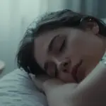 Mujer durmiendo plácidamente con sensores de monitoreo fisiológico en rostro y muñeca, en un dormitorio con luz tenue y ambiente sereno.