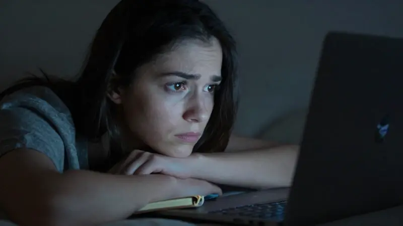 Joven preocupada mirando la pantalla de un portátil en la oscuridad, posiblemente buscando el significado de un sueño.