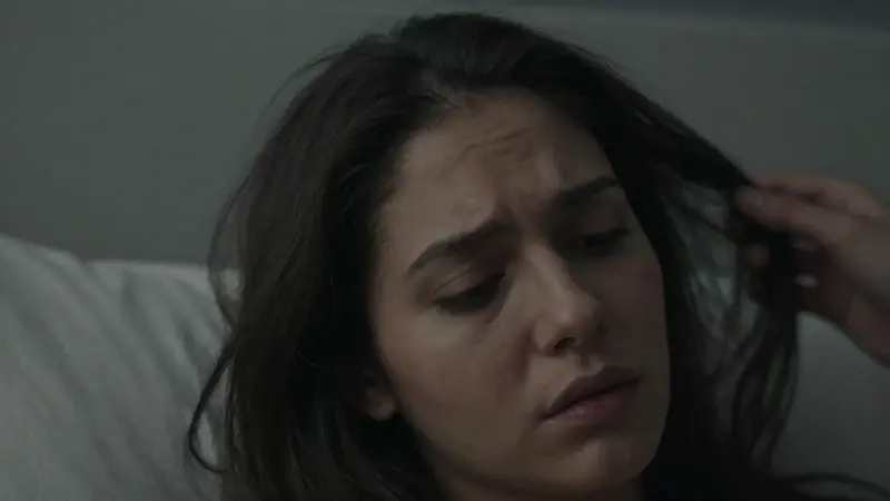 Primer plano de la cabeza de una mujer con el pelo oscuro, mostrando sutiles indicios de movimiento en el cabello, en un dormitorio tenuemente iluminado.