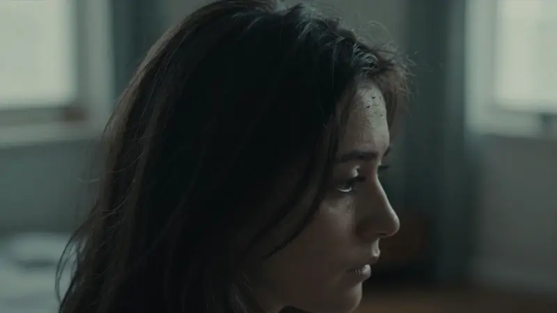 Primer plano de una mujer de perfil con el cabello oscuro y enredado, en una habitación tenuemente iluminada, con pequeñas formas oscuras que sugieren piojos. Ambiente ansioso y melancólico.