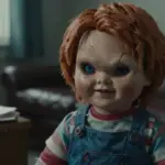 Primer plano de una muñeca Chucky de porcelana desgastada, con pintura agrietada y una mirada inquietante, en el interior de un consultorio de terapeuta tenuemente iluminado.