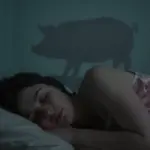 Mujer durmiendo en un dormitorio tenuemente iluminado, con la sombra sutil de un cerdo proyectada en la pared.