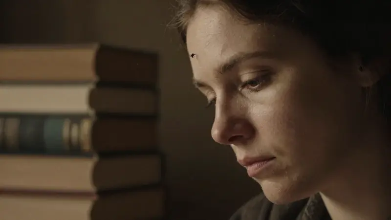 Mujer pensativa en una biblioteca antigua, con una mosca aterrizando sutilmente en su sien. Ambiente melancólico e introspectivo.