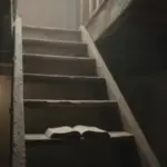 Escalera de madera en ático polvoriento, iluminada por una bombilla, ascendiendo hacia la oscuridad. Un libro antiguo descansa sobre uno de los peldaños.