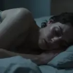 Persona angustiada durmiendo en una habitación con iluminación dramática y tonos oscuros, sugiriendo una atmósfera de pesadilla o terror nocturno.