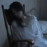 Aparición etérea de una mujer translúcida en un dormitorio antiguo con una mecedora de madera y papel tapiz floral desgastado.
