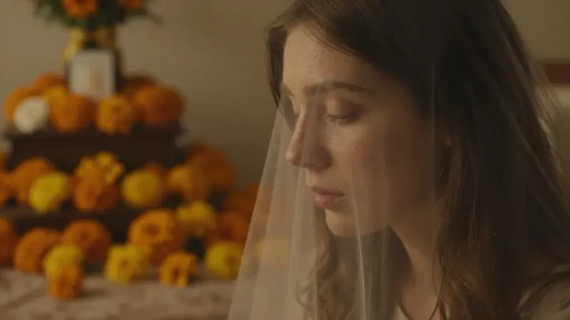 Rostro femenino semitransparente desvaneciéndose en flores de cempasúchil, con un ambiente melancólico y cálido en un dormitorio tenuemente iluminado.