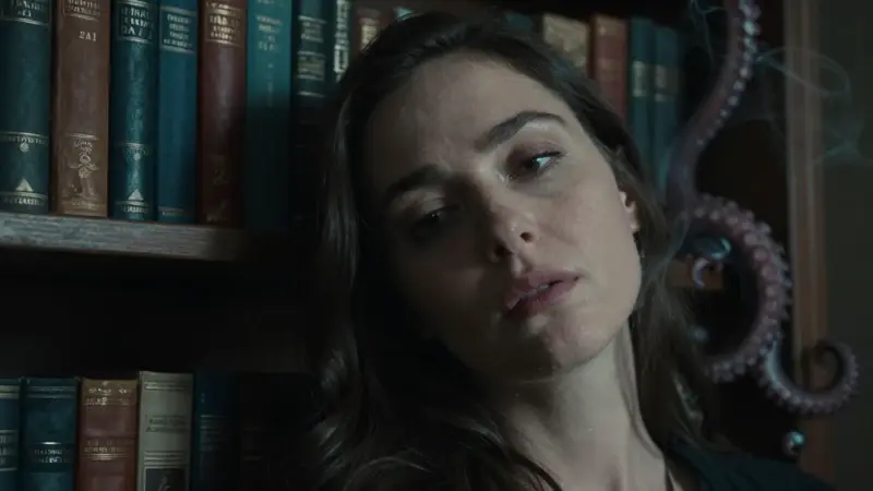 Mujer pensativa en un estudio antiguo con libros y elementos decorativos con forma de tentáculos de pulpo, evocando una atmósfera melancólica y onírica.