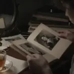 Mujer mirando un álbum de fotos antiguo en un estudio tenuemente iluminado, rodeada de diarios de sueños y una taza de té. Ambiente melancólico e introspectivo.