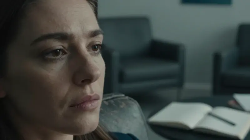 Primer plano de una mujer con mirada intensa en un ambiente que sugiere una consulta terapéutica, rodeada de diarios de sueños.