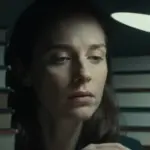 Mujer concentrada e iluminada por una lámpara, rodeada de libros de psicología en un estudio oscuro y melancólico, reflejando la introspección y el análisis de los sueños.