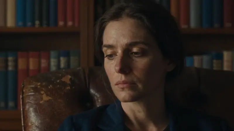 Mujer pensativa en un estudio con estanterías llenas de libros de psicología, evocando una atmósfera serena e intelectual. El enfoque está en sus ojos, transmitiendo introspección y contemplación.